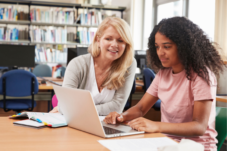 Docent en student samen aan tafel terwijl ze iets op de laptop bekijken